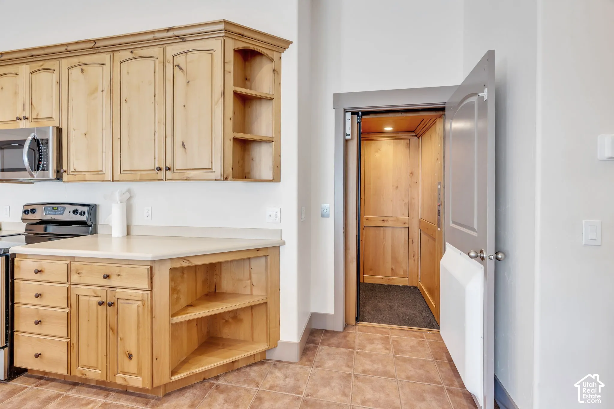 Kitchen area featuring light wood cabinetry with open shelving, stainless steel microwave, and an electric range