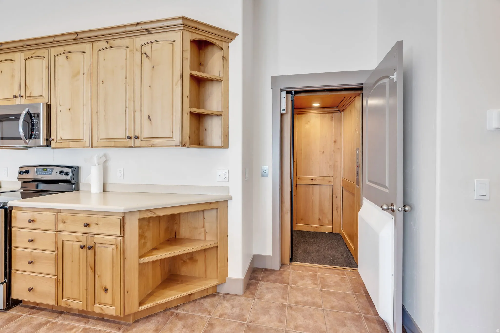 Kitchen area featuring light wood cabinetry with open shelving, stainless steel microwave, and an electric range