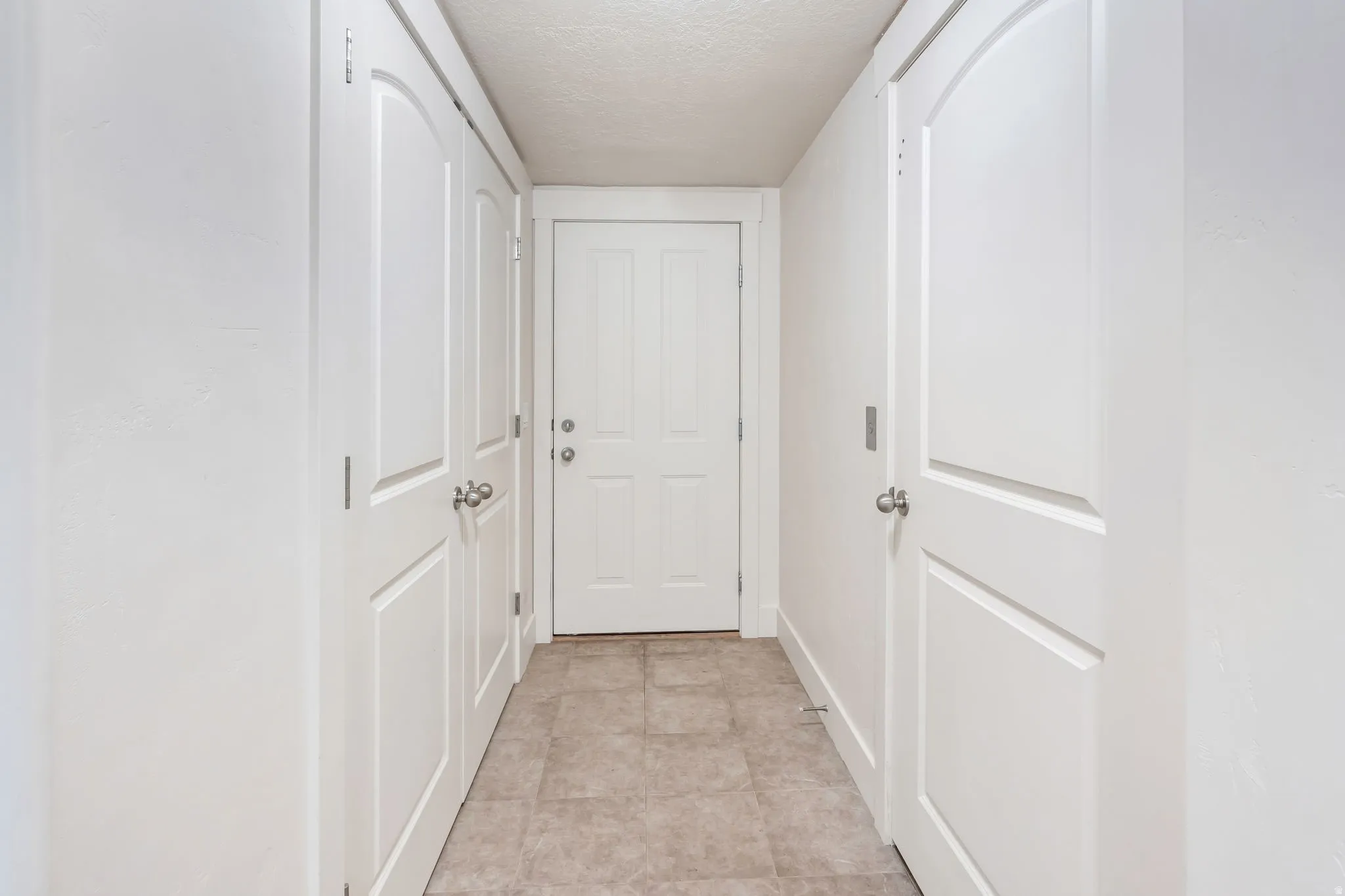 Hallway featuring neutral-toned tile flooring and white paneled doors with brushed nickel hardware