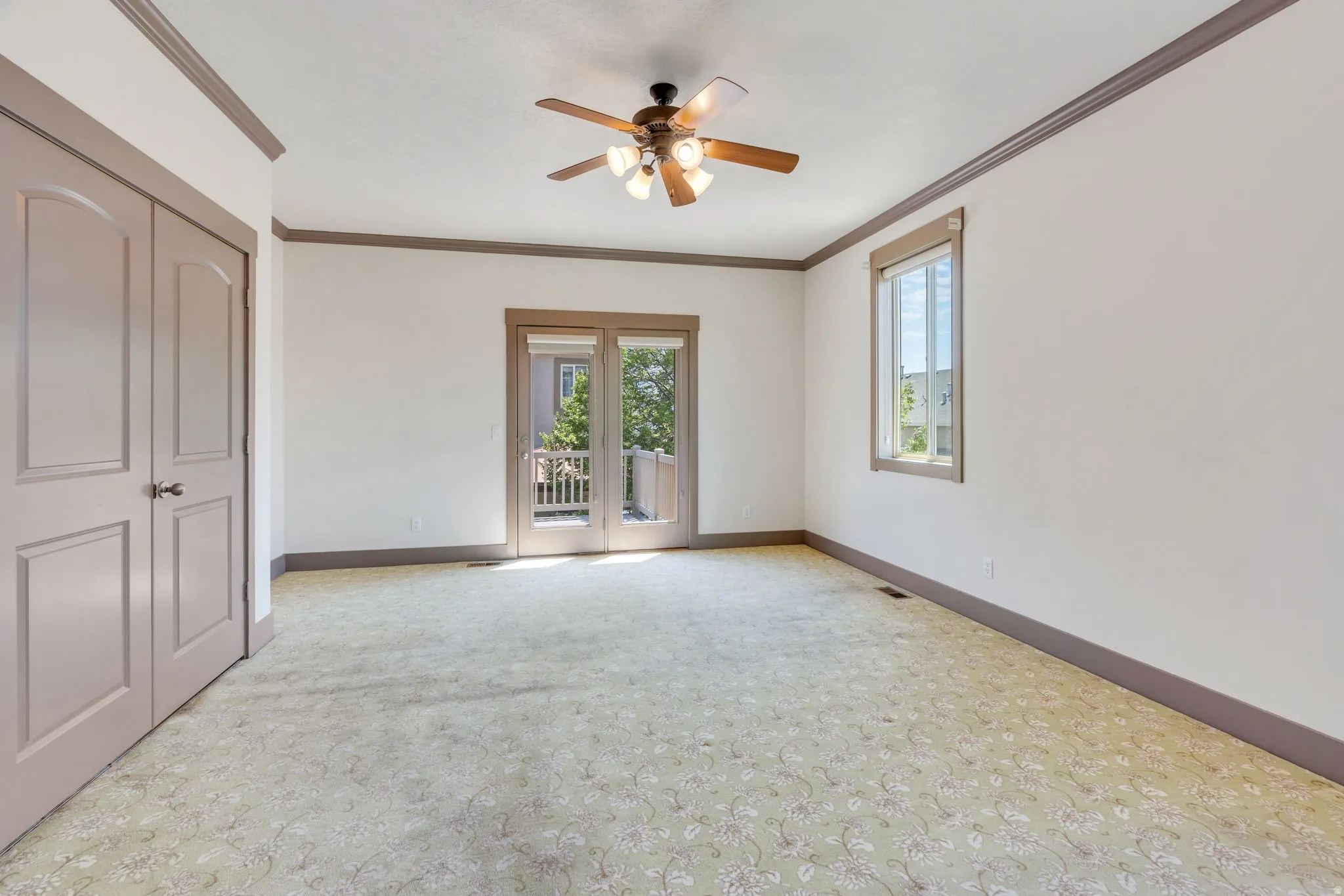 Spacious room featuring patterned carpeting, ceiling fan with light fixture, and crown molding