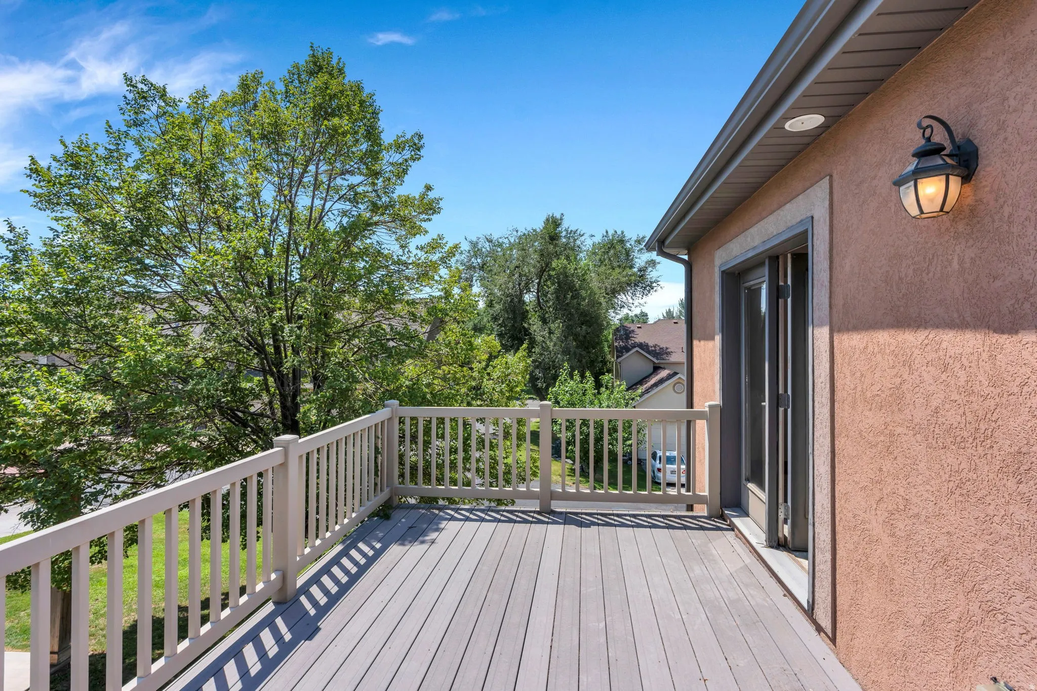 Expansive outdoor deck featuring wood-finish flooring, a full railing, and exterior wall sconce