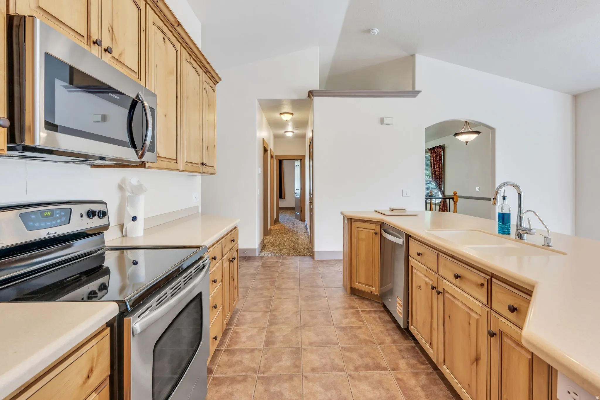 Kitchen featuring wood cabinetry, stainless steel appliances, light-toned countertops, and tile flooring