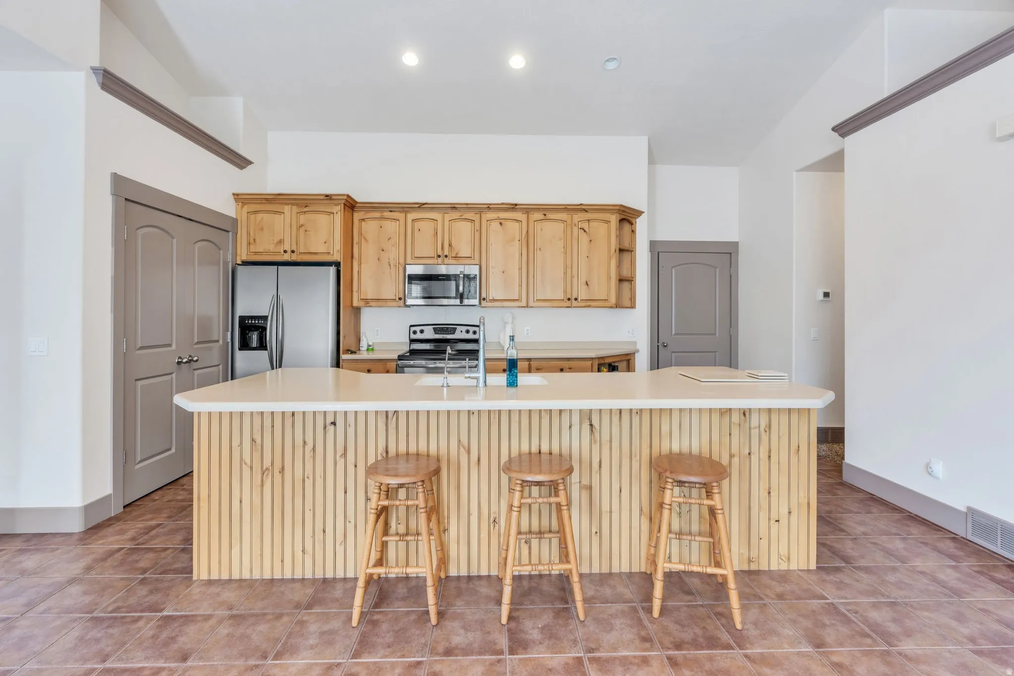 Kitchen featuring natural wood cabinetry, stainless steel appliances, a large island with a light-toned countertop, and durable tile flooring