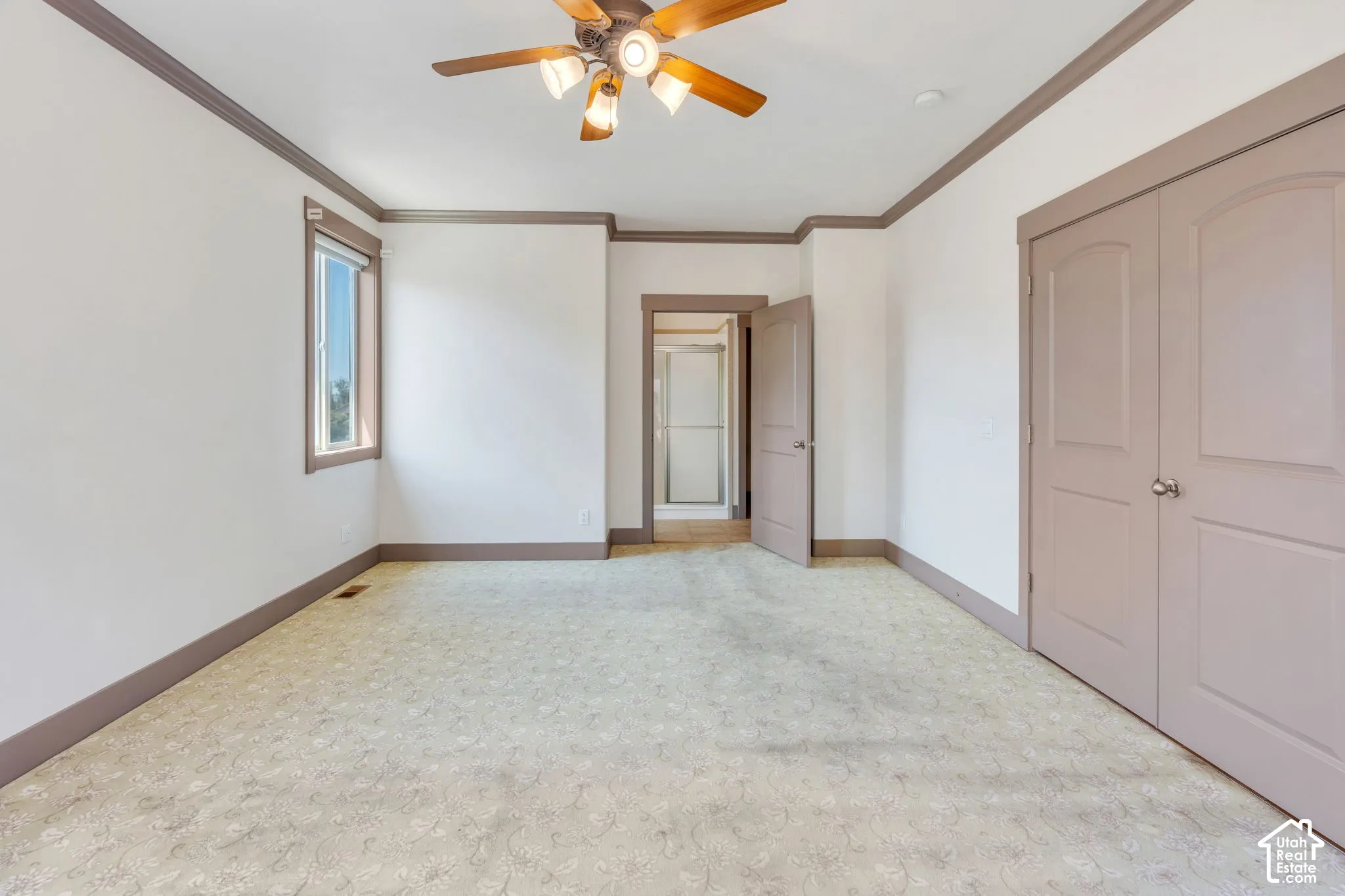 Spacious room featuring neutral carpeting, a ceiling fan with integrated lighting, and a single window with trim
