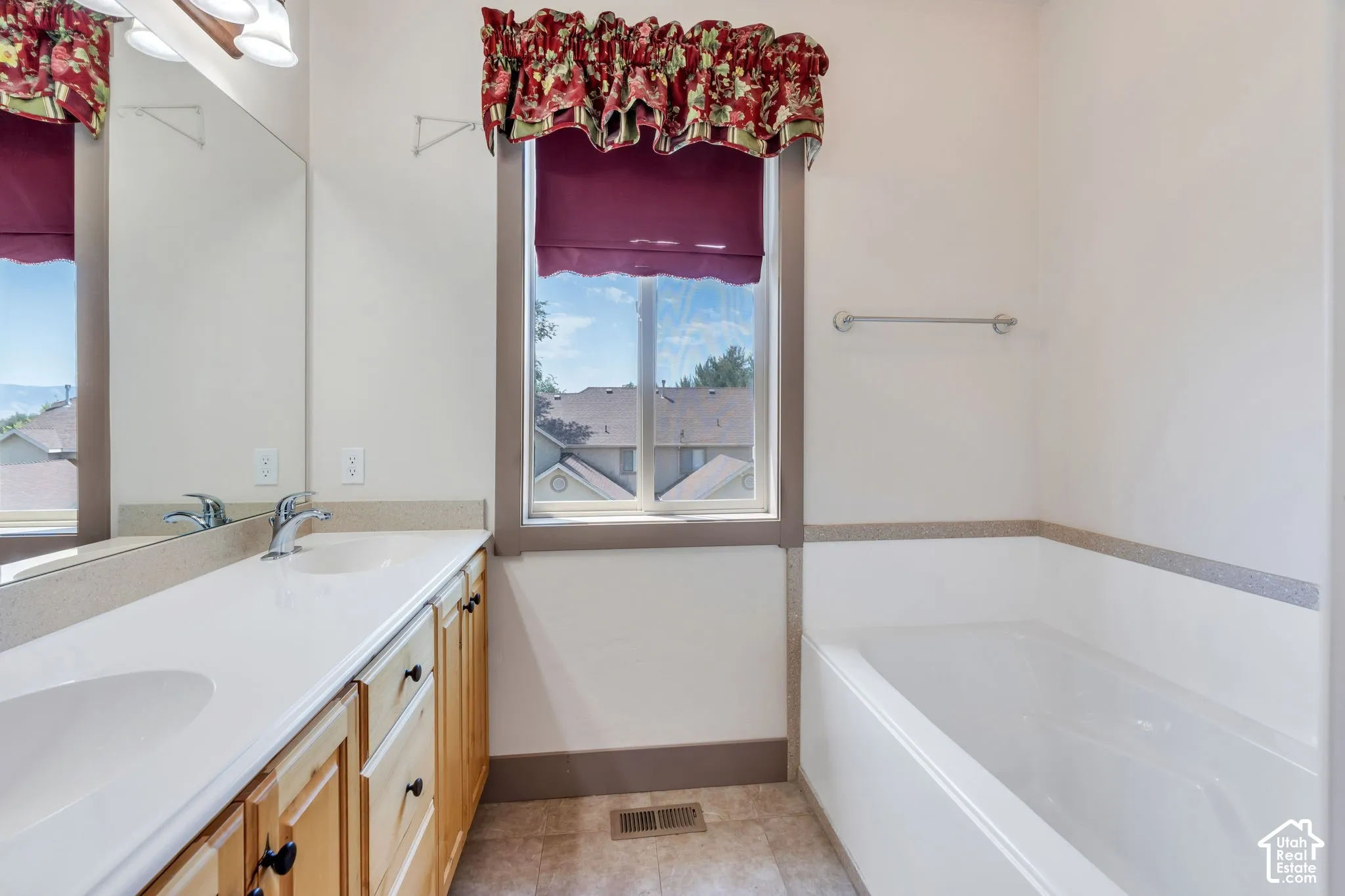 Bathroom featuring a double vanity with light wood cabinetry, a built-in bathtub, and a window