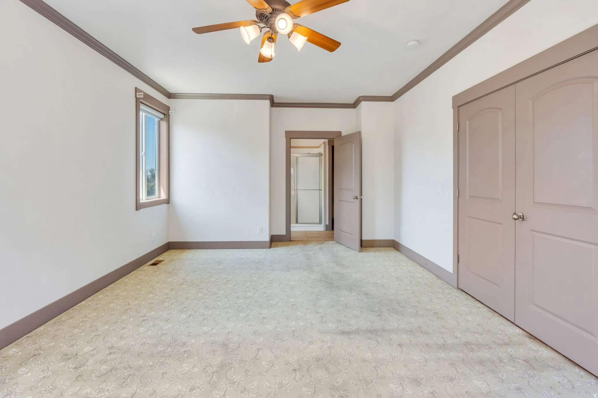 Spacious room featuring neutral carpeting, a ceiling fan with integrated lighting, and a single window with trim