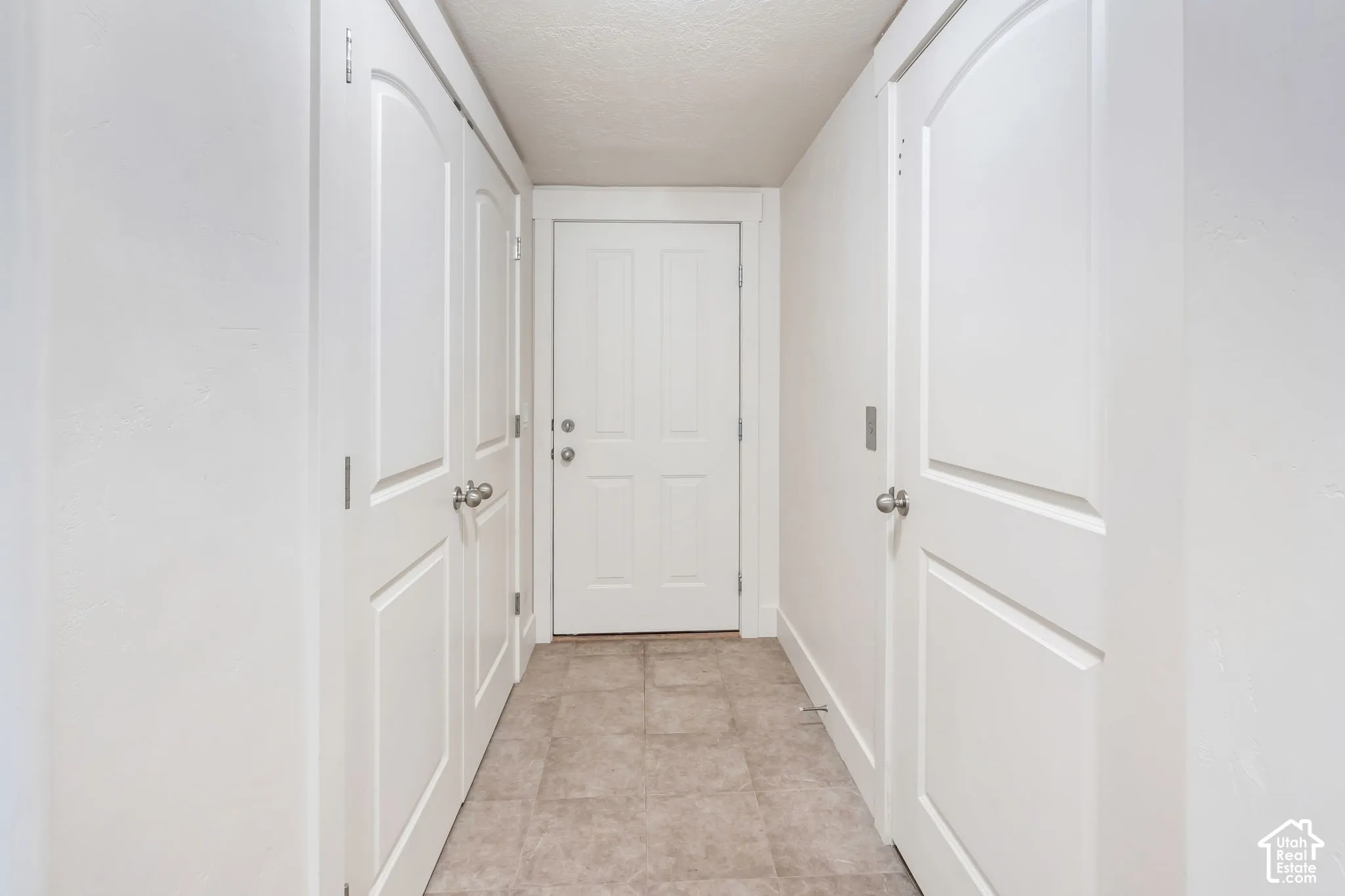 Hallway featuring neutral-toned tile flooring and white paneled doors with brushed nickel hardware