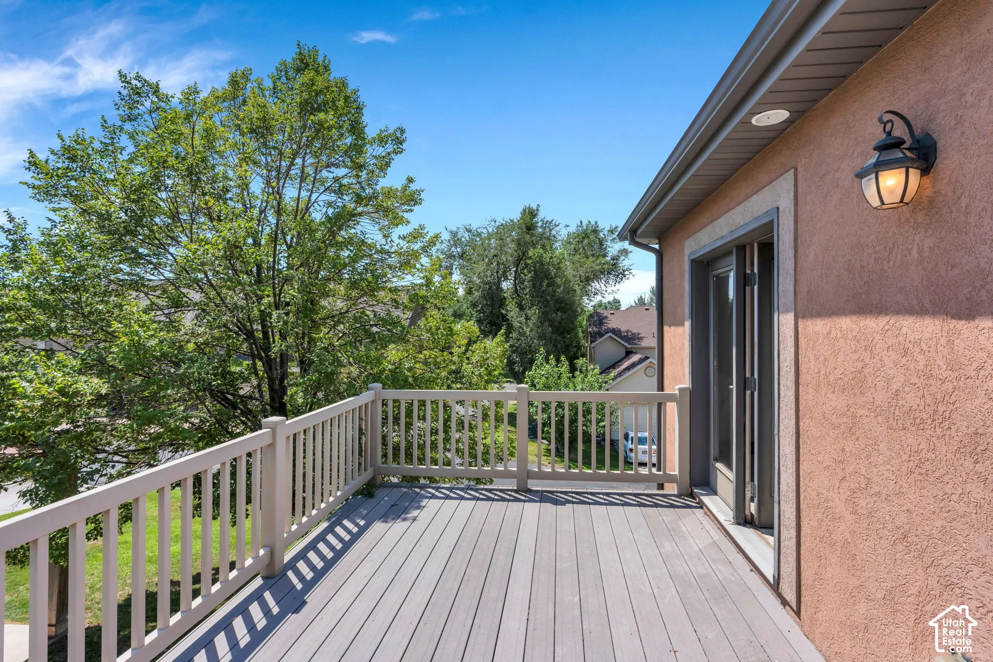Expansive outdoor deck featuring wood-finish flooring, a full railing, and exterior wall sconce