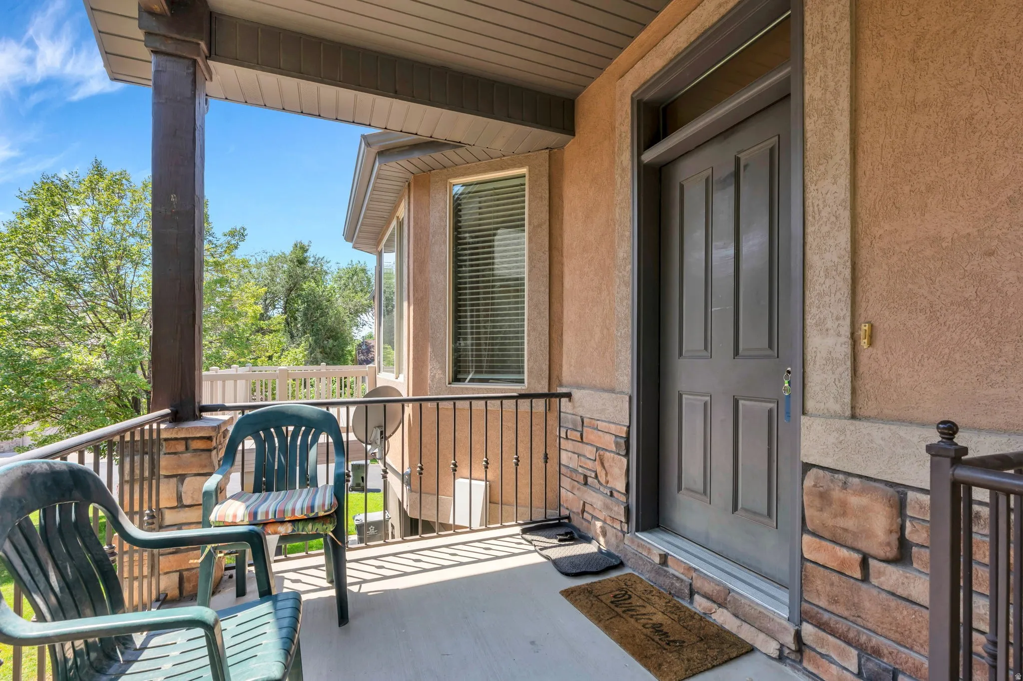 Covered front porch featuring a paneled entry door with transom window, stone veneer accents, stucco exterior, and black metal railing
