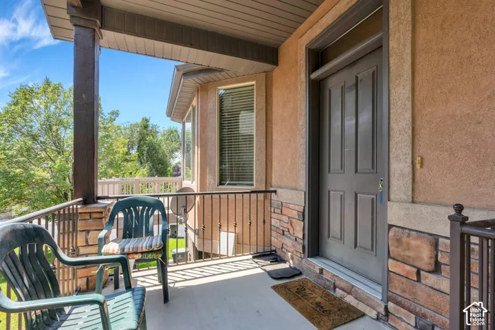 Covered front porch featuring a paneled entry door with transom window, stone veneer accents, stucco exterior, and black metal railing