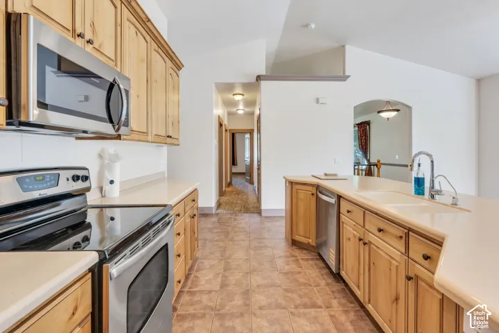Kitchen featuring wood cabinetry, stainless steel appliances, light-toned countertops, and tile flooring