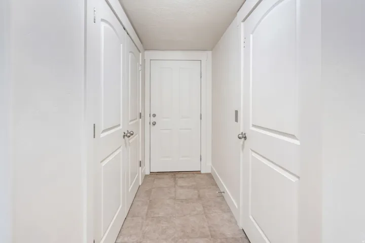 Hallway featuring neutral-toned tile flooring and white paneled doors with brushed nickel hardware