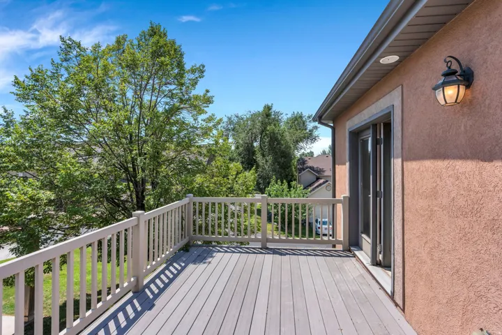 Expansive outdoor deck featuring wood-finish flooring, a full railing, and exterior wall sconce