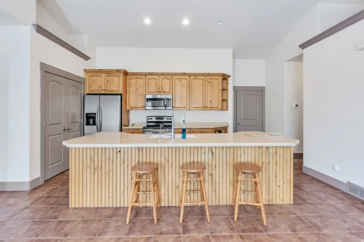 Kitchen featuring natural wood cabinetry, stainless steel appliances, a large island with a light-toned countertop, and durable tile flooring