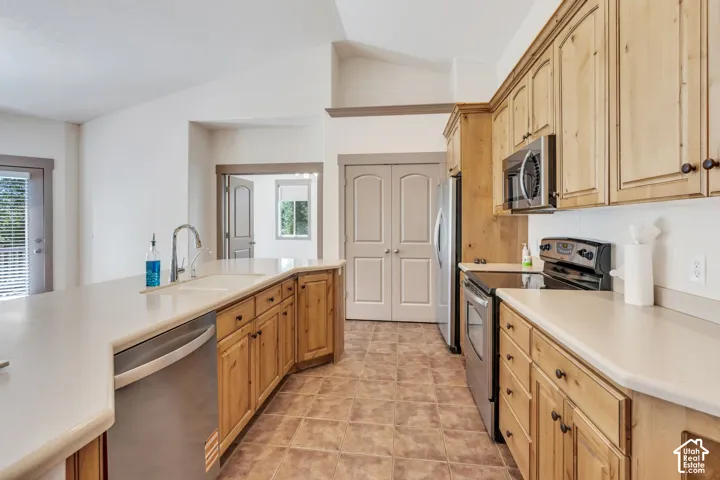Kitchen featuring wood-finish cabinetry, stainless steel appliances, light-toned countertops, tile flooring, and vaulted ceilings