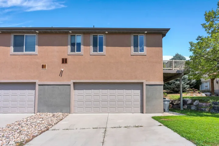 Multi-level stucco exterior featuring an integrated garage, upper-level windows, and a raised wood deck