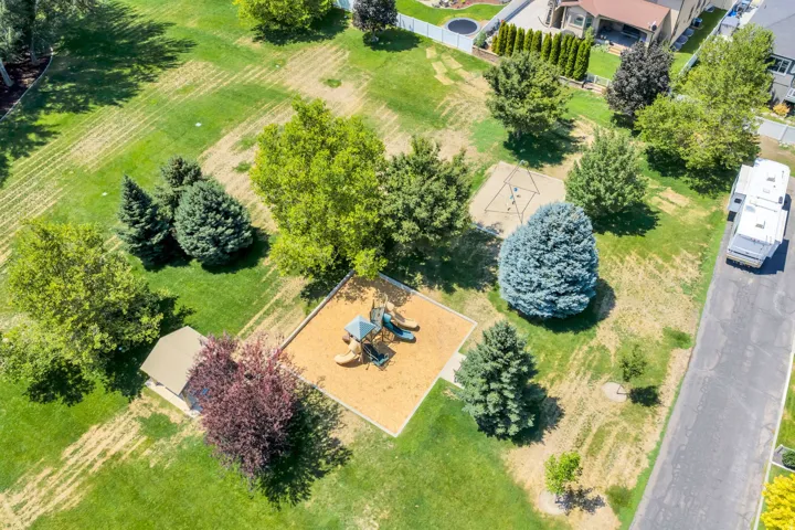 Expansive green space featuring a playground with wood chip surfacing, a swing set, mature trees, and a small outbuilding with a brown shingled roof