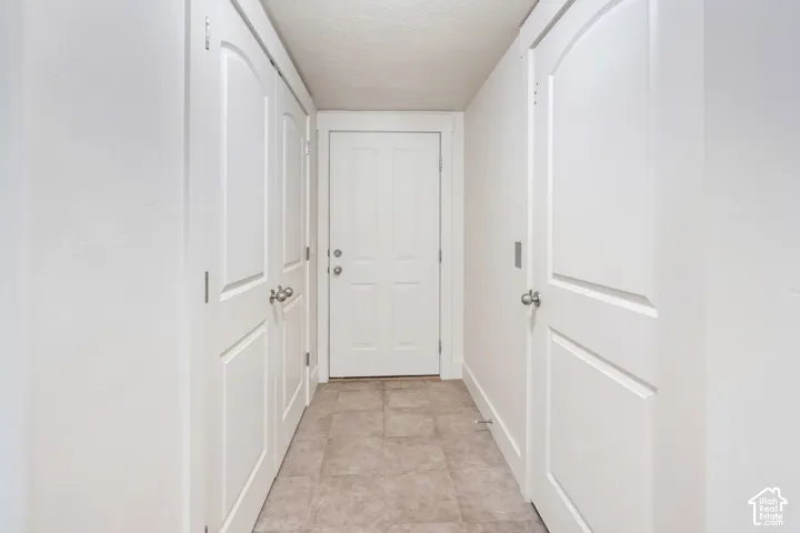 Hallway featuring neutral-toned tile flooring and white paneled doors with brushed nickel hardware