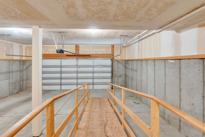 Spacious garage featuring a motorized overhead door, concrete slab flooring, and a built-in wooden ramp with handrails