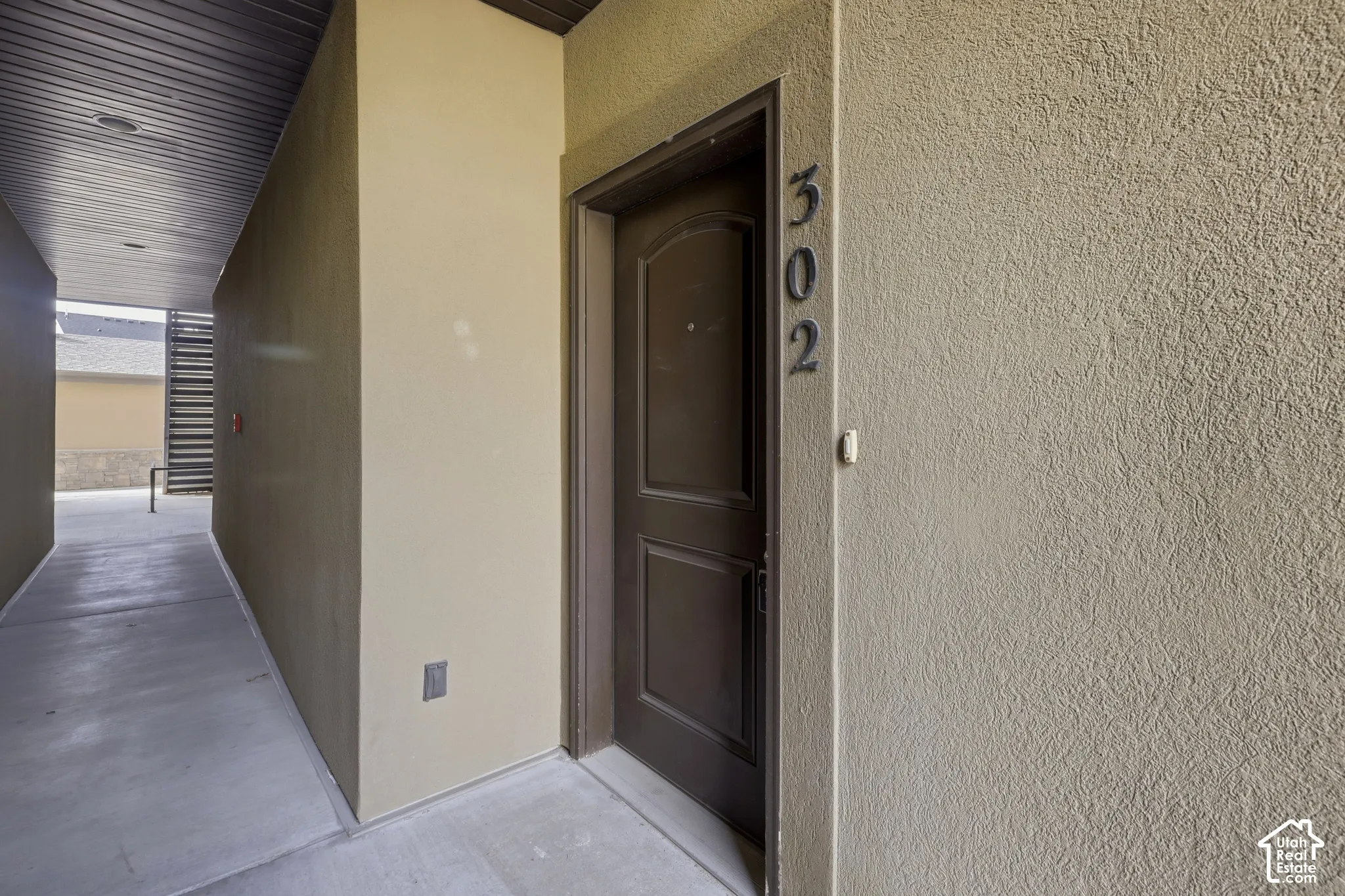 Exterior entry featuring a textured stucco facade, covered walkway, recessed ceiling lighting, and a solid-panel door with architectural hardware
