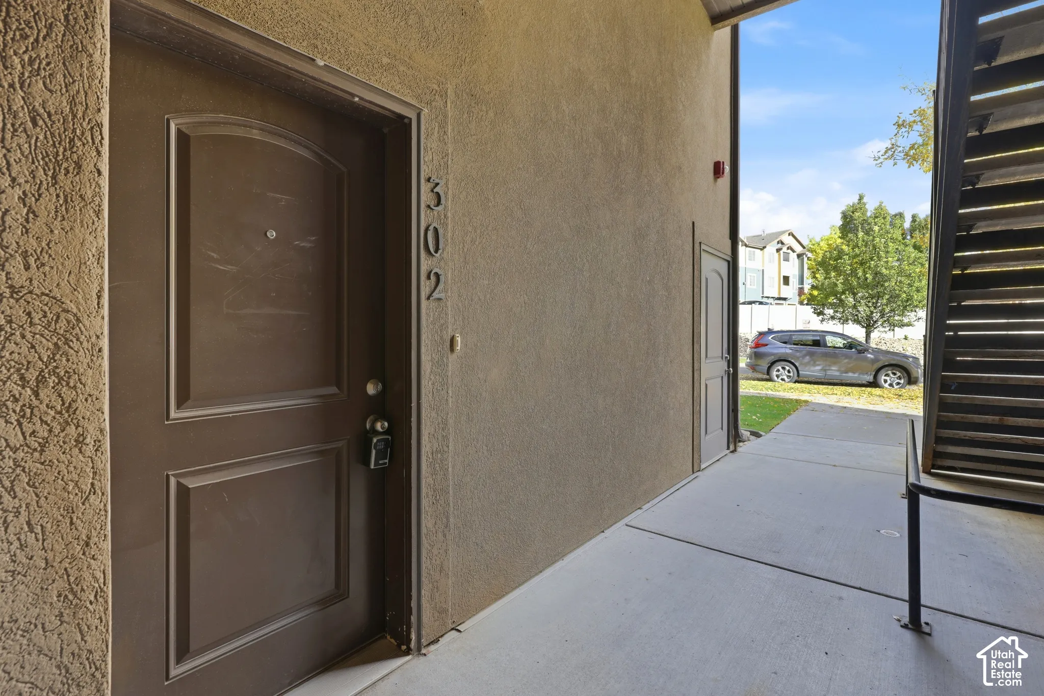 Stucco exterior entrance featuring a paneled entry door, concrete walkway, and metal staircase