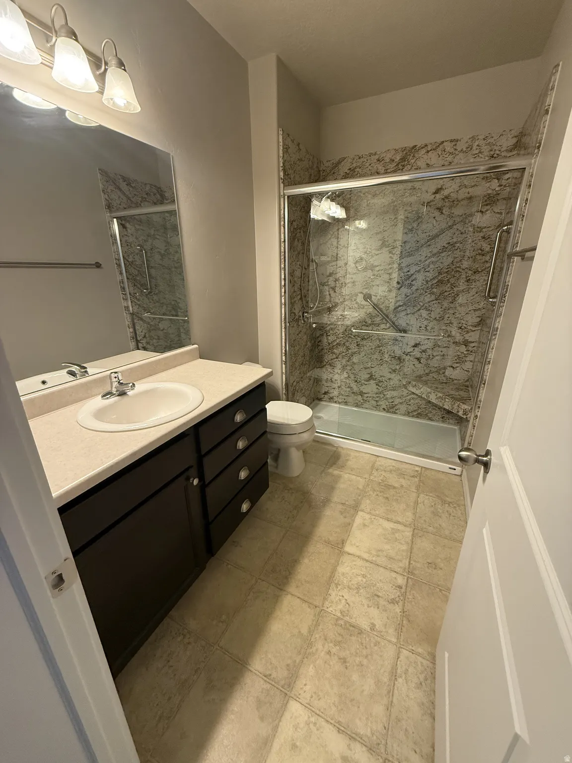 Bathroom featuring a built-in vanity with a countertop and undermount sink, a shower enclosure with patterned wall panels and a sliding glass door, and tiled flooring