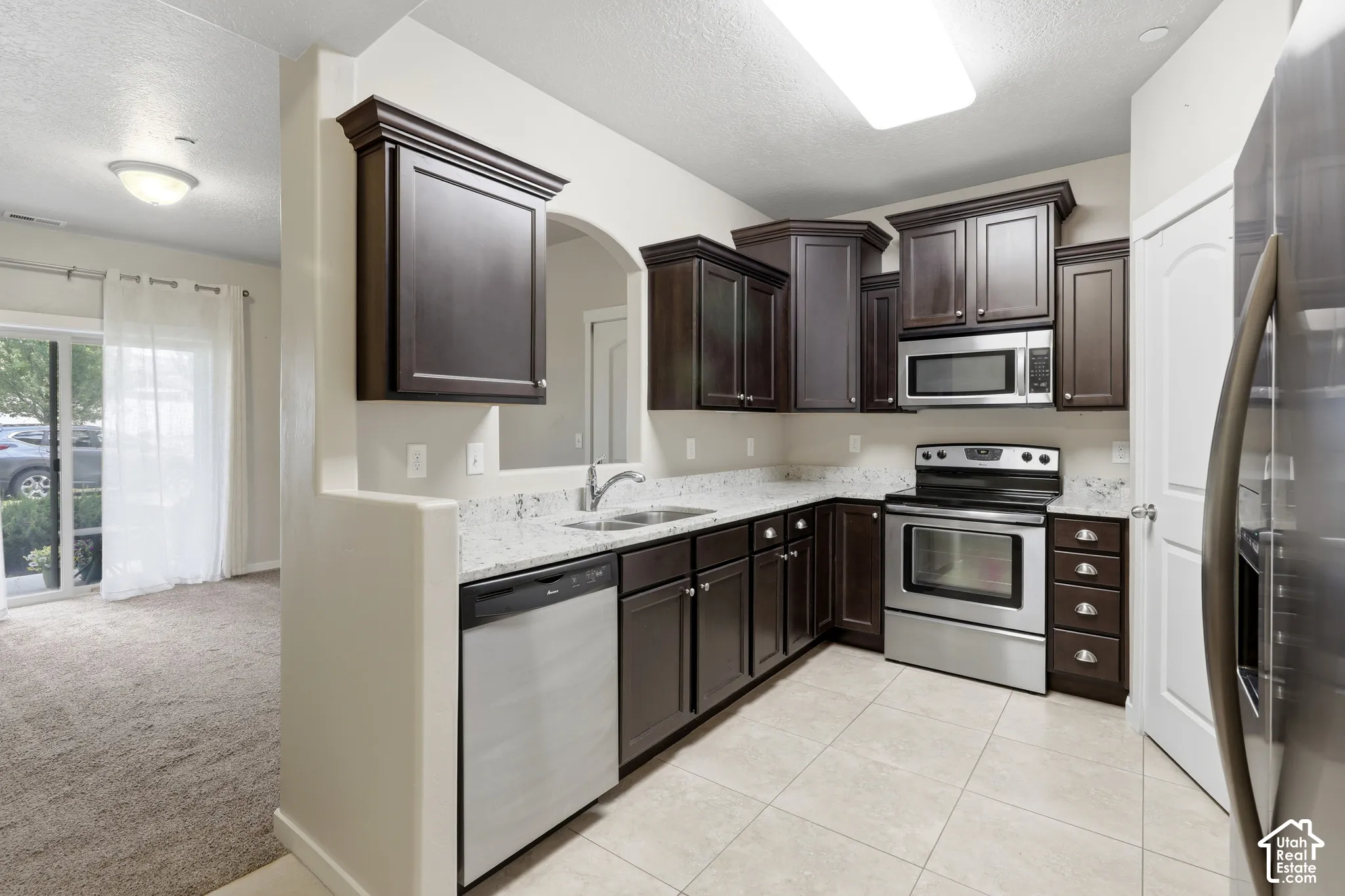 Kitchen featuring dark-finish cabinetry, stone-look countertops, stainless steel appliances, and ceramic tile flooring