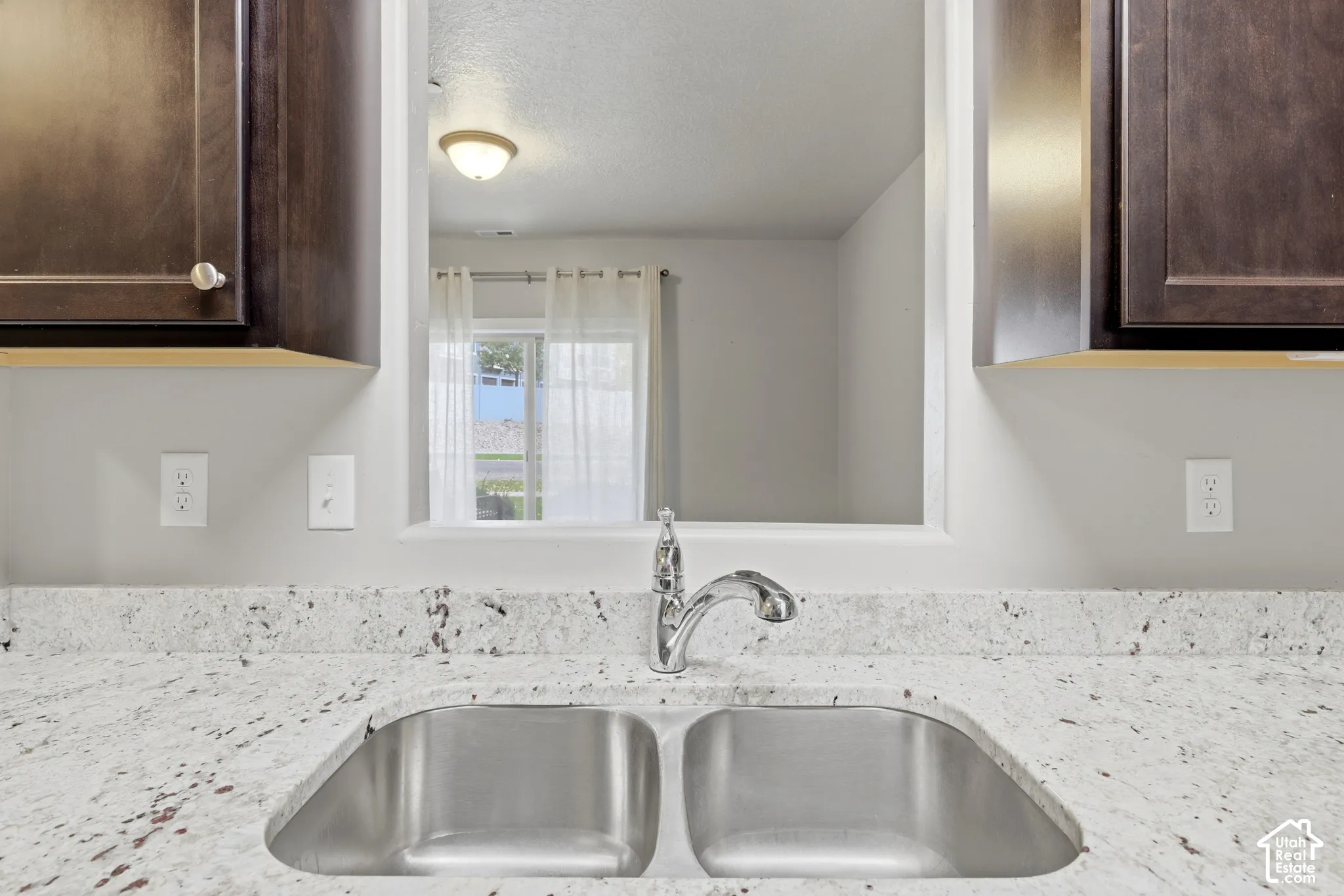 Double-basin stainless steel sink with high-arc chrome faucet, speckled stone countertop, and dark wood-finish cabinetry