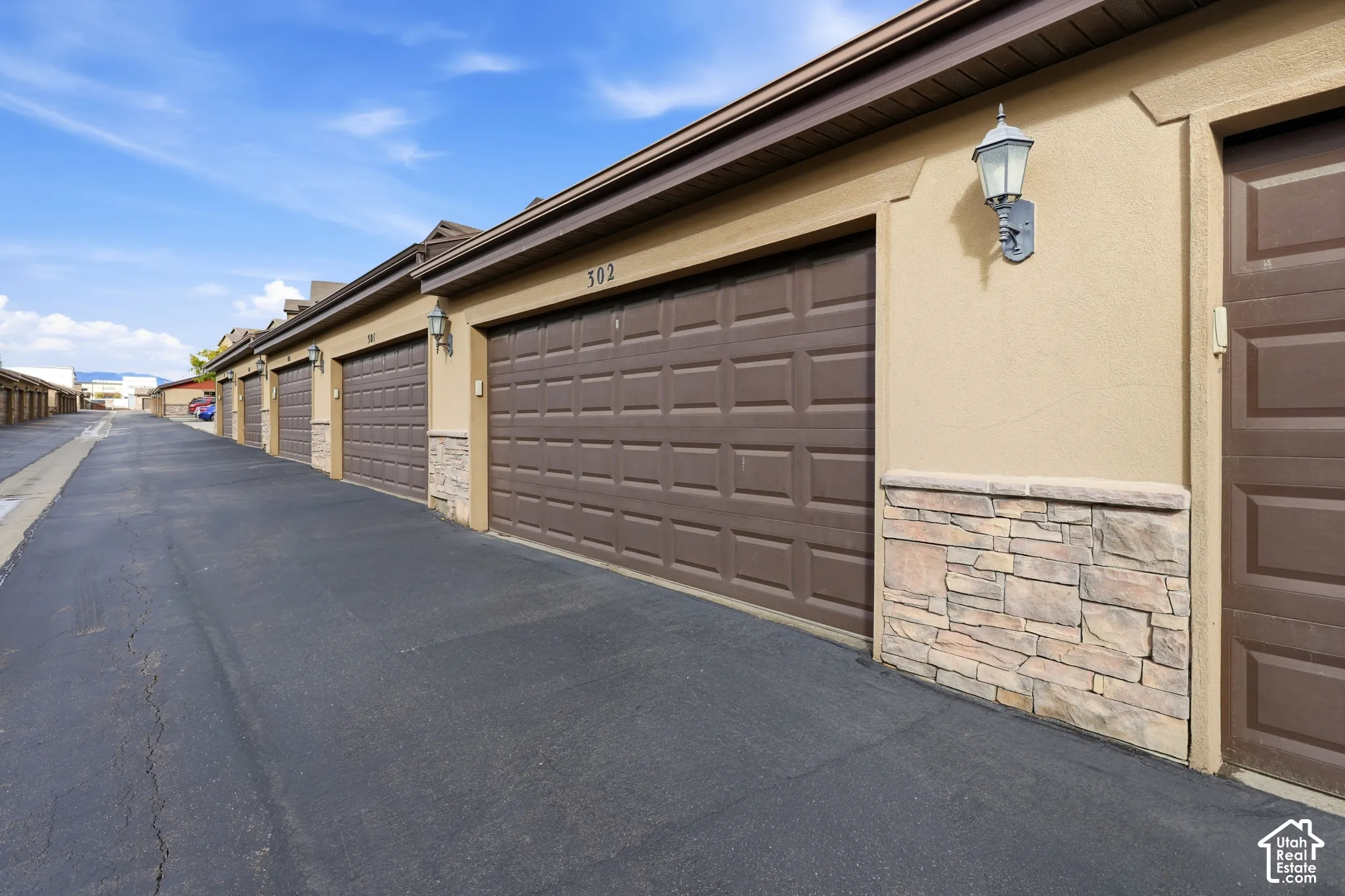 Detached garage block featuring tan stucco siding, stacked stone accents, brown paneled doors, and exterior wall-mounted carriage lights