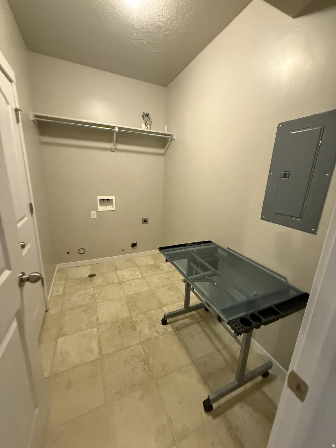 Utility room featuring light-toned tile flooring, neutral wall paint, and a built-in wire shelf with hanging rod