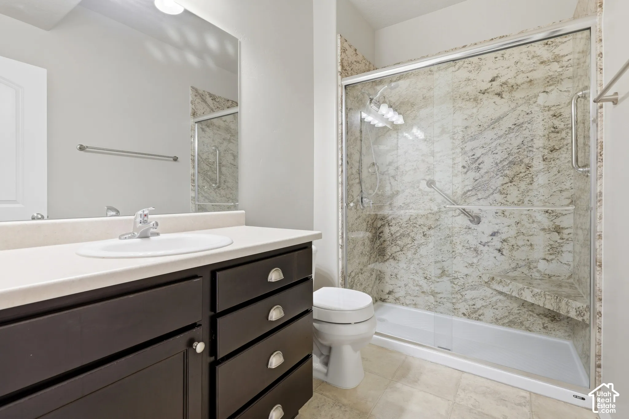 Bathroom featuring a dark wood-finish vanity with a light-toned countertop, a glass-enclosed shower with full-height stone-patterned wall surrounds, built-in shower seating, and a large wall-mounted mirror