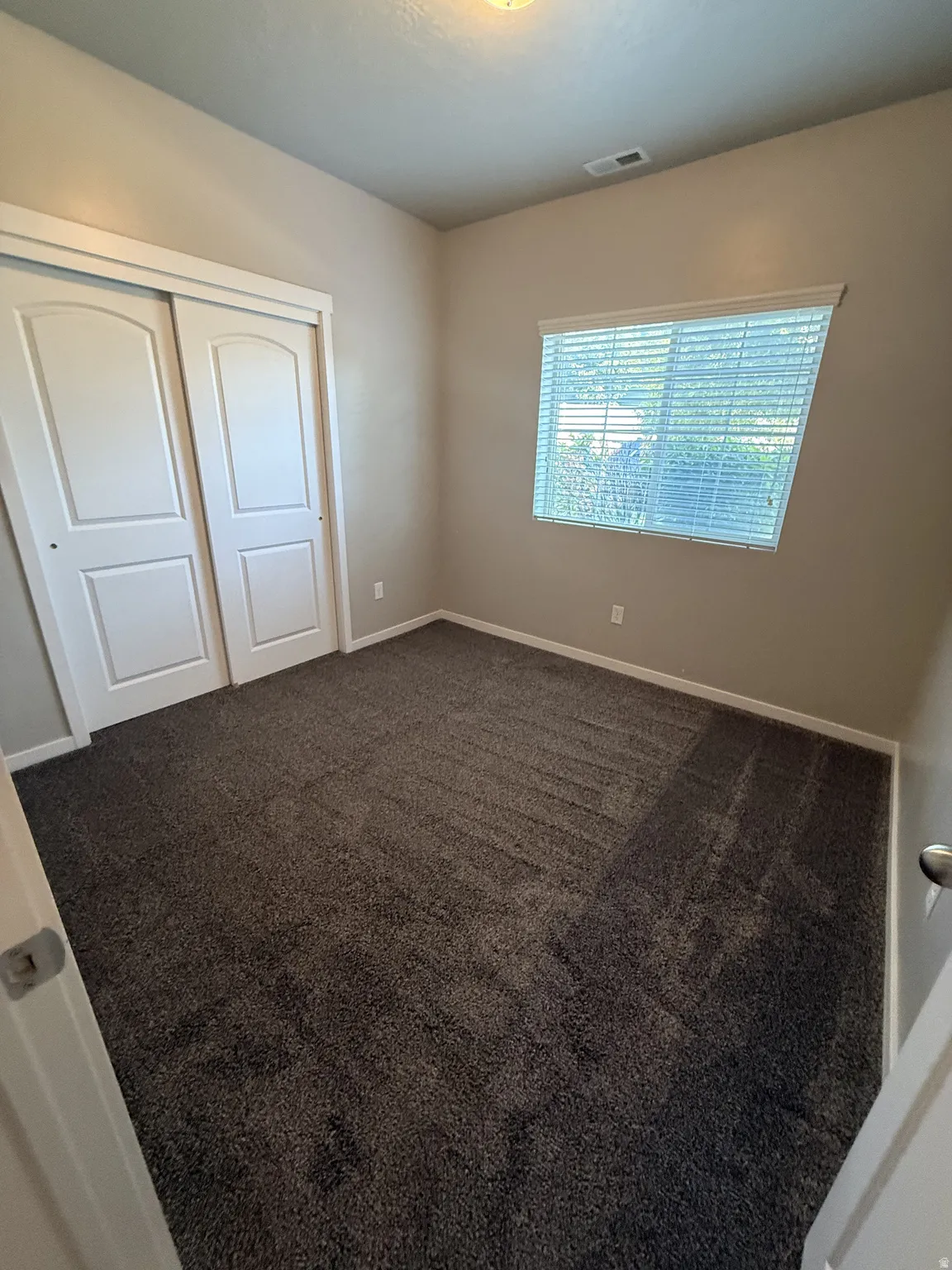 Bedroom featuring textured gray carpeting, neutral wall paint, and a window with horizontal blinds