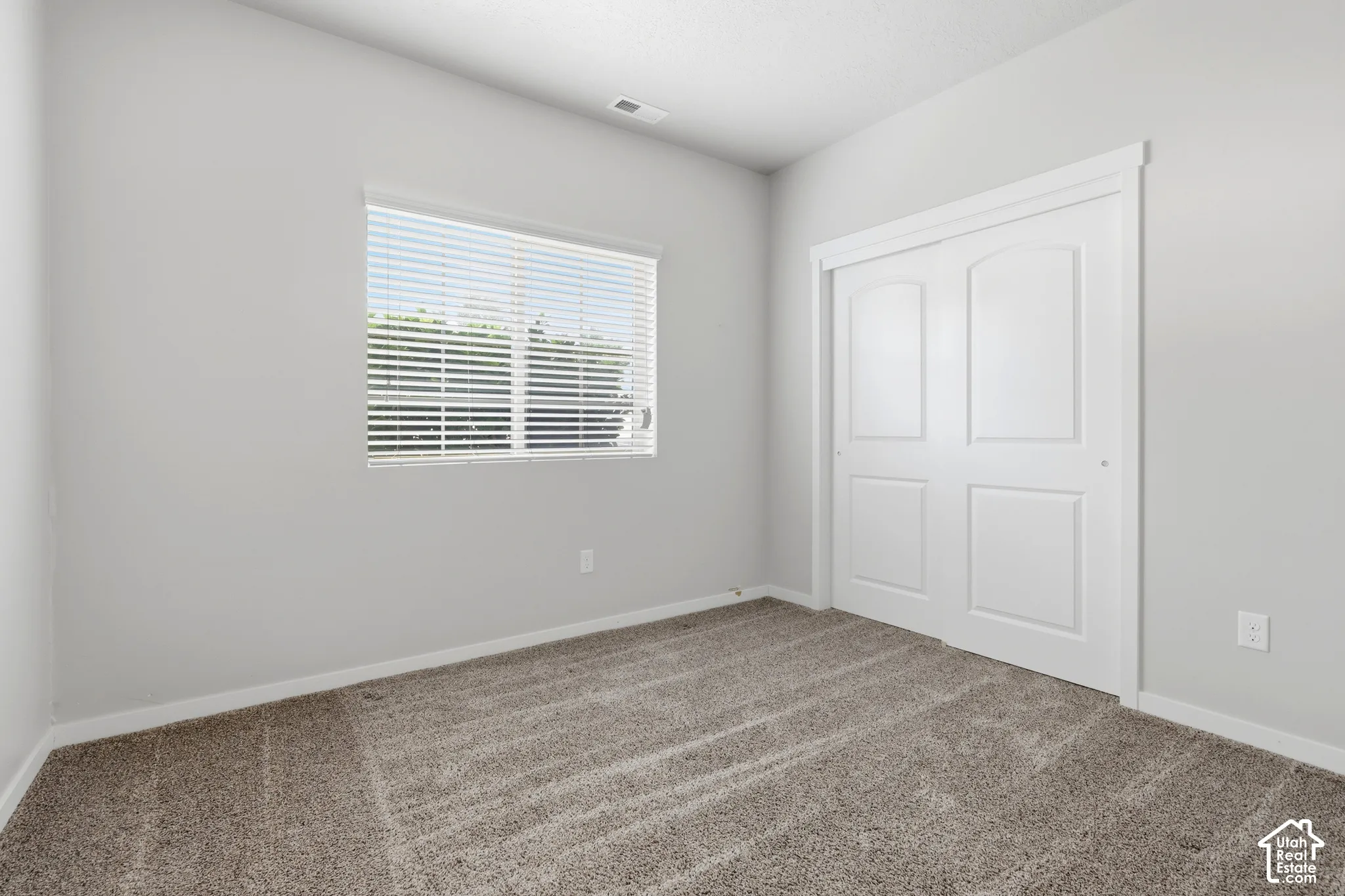 Neutral-toned interior room featuring wall-to-wall carpeting, a window with horizontal blinds, and a white dual-panel sliding closet door