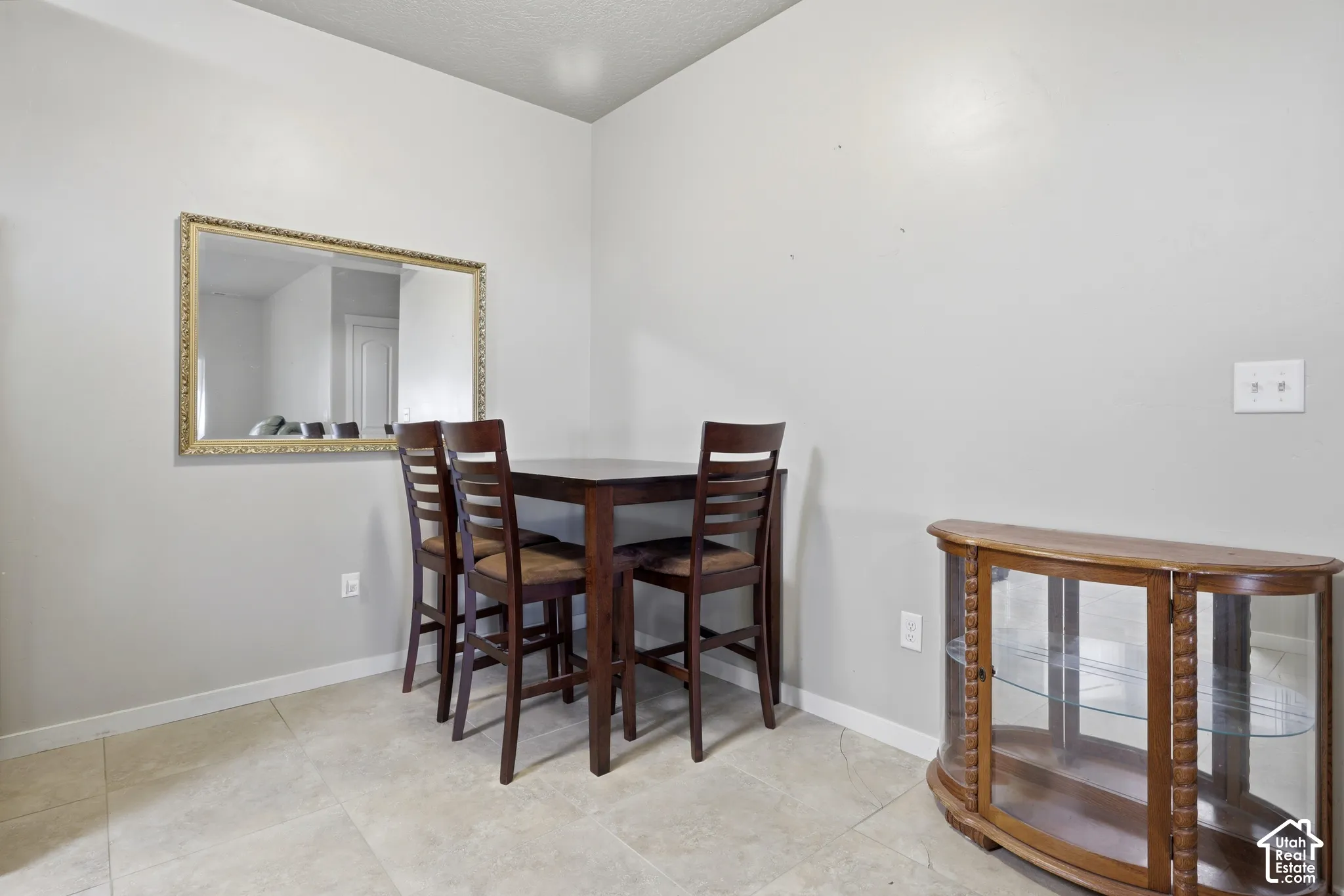 Neutral-toned interior space featuring light-colored stone-finish floor tiling and a wall-mounted rectangular mirror with a decorative gold-tone frame