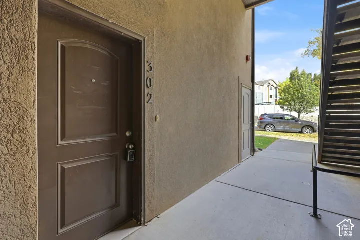 Stucco exterior entrance featuring a paneled entry door, concrete walkway, and metal staircase