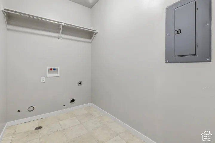 Utility space featuring ceramic tile flooring, built-in overhead shelving, electrical service panel, and dedicated plumbing hookups