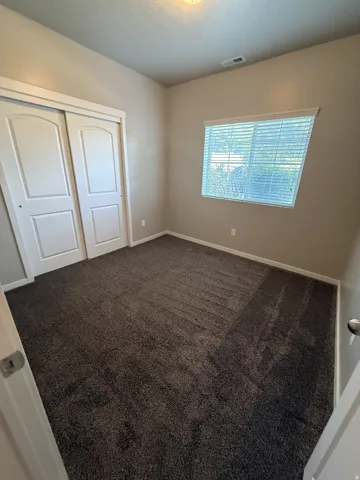 Bedroom featuring textured gray carpeting, neutral wall paint, and a window with horizontal blinds