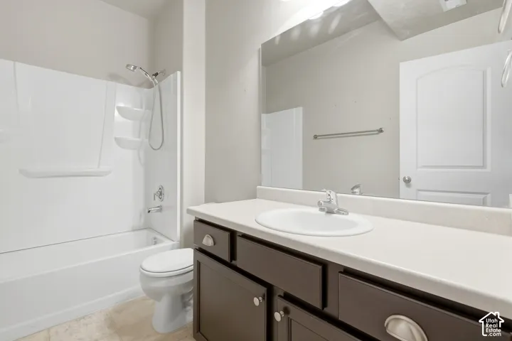 Bathroom featuring a dark-toned vanity with a white countertop and oval undermount sink, a shower-tub combination with white surround, and a large wall-mounted mirror