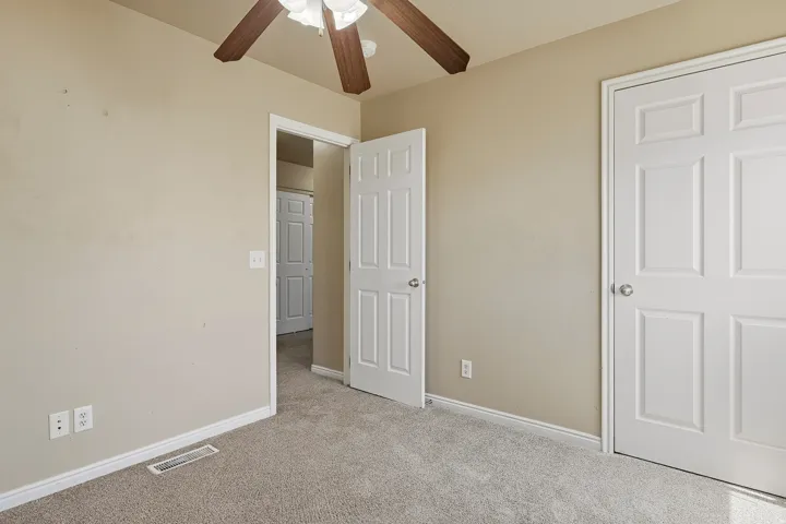 Carpeted room featuring a ceiling fan with light fixture, six-panel interior doors, and neutral wall paint