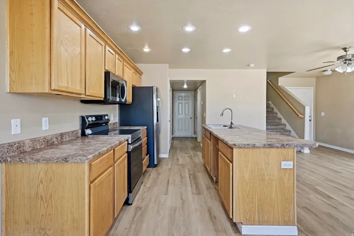 Kitchen featuring wood-finish cabinetry, speckled countertops, stainless steel appliances, and an island with an integrated sink and breakfast bar