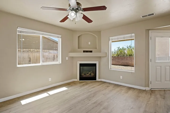 Living area featuring a built-in fireplace with mantel, recessed display niche, two windows with blinds, wood-finish flooring, and a ceiling fan