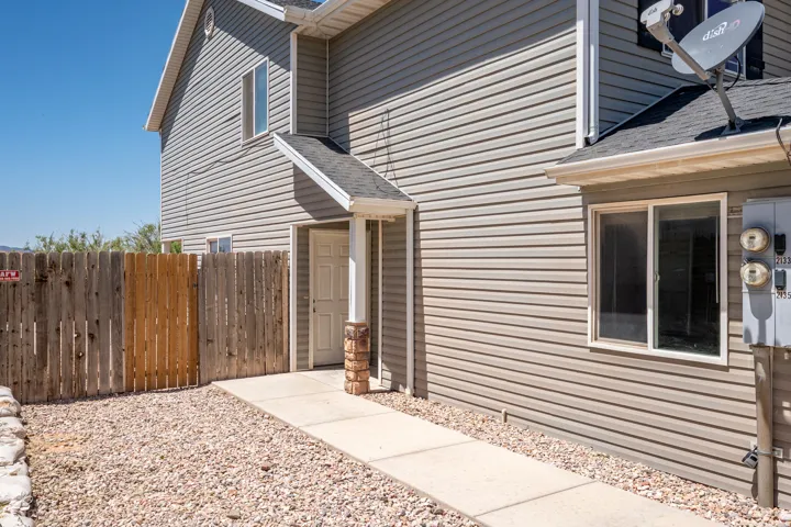 Exterior featuring tan horizontal siding, a covered entry with a decorative column, a privacy fence, a concrete walkway, and gravel landscaping