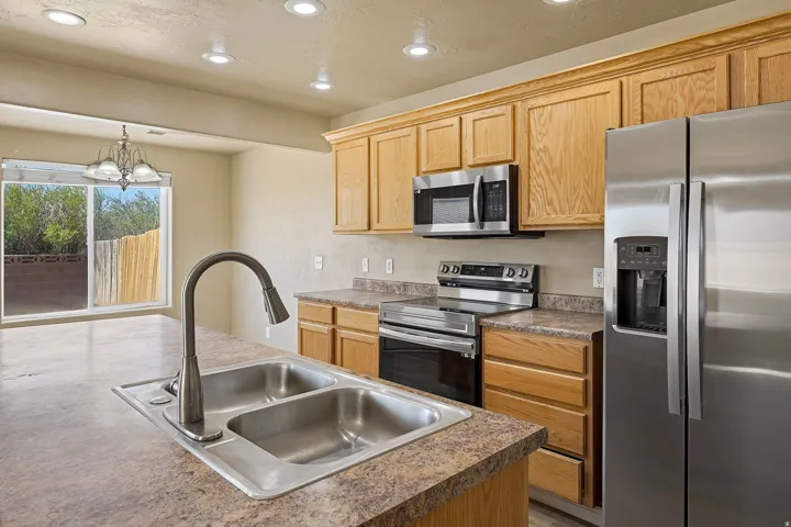 Kitchen featuring a double basin sink with a gooseneck faucet, light wood cabinetry, stainless steel appliances, recessed ceiling lighting, and a sliding glass door