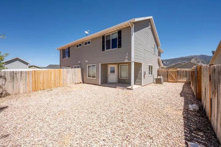Rear exterior featuring gray horizontal siding, a gravel-covered yard, and full perimeter wood fencing