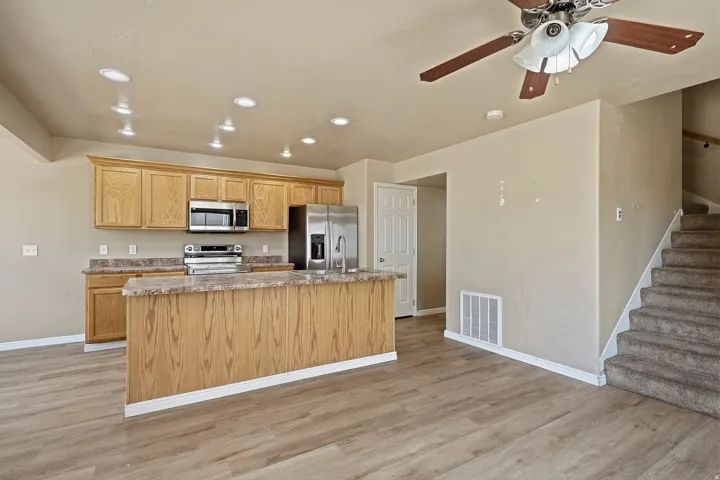 Kitchen with light wood cabinetry, stainless steel appliances, and a large island featuring a stone-look countertop