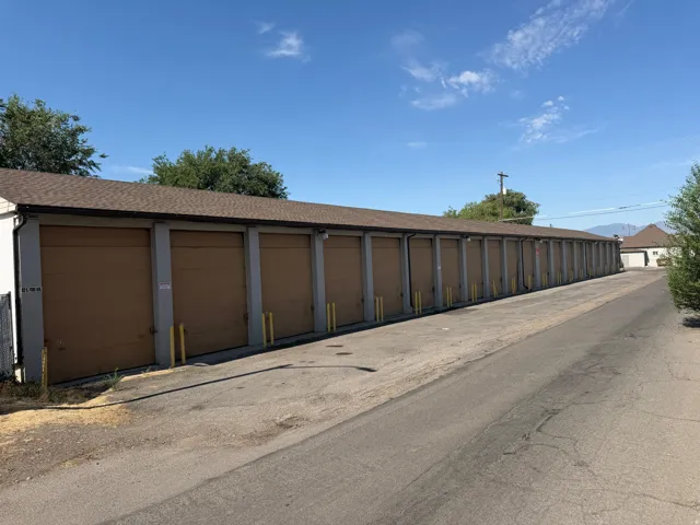 Long row of storage units featuring brown roll-up doors and individual security bollards