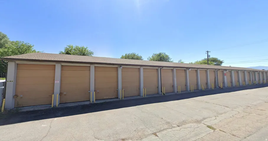 Long row of individual storage units featuring tan roll-up doors, concrete framing, and a shingled roofline