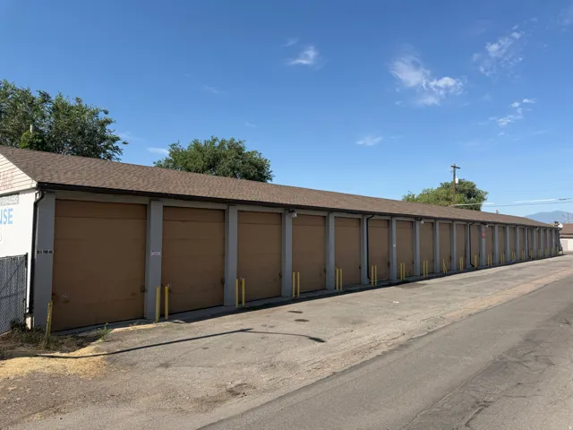 Long single-story storage facility featuring numerous individual bay doors, a brown shingle roof, and a paved access drive