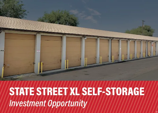 Row of multiple self-storage units with roll-up doors, individual security bollards, and asphalt pavement