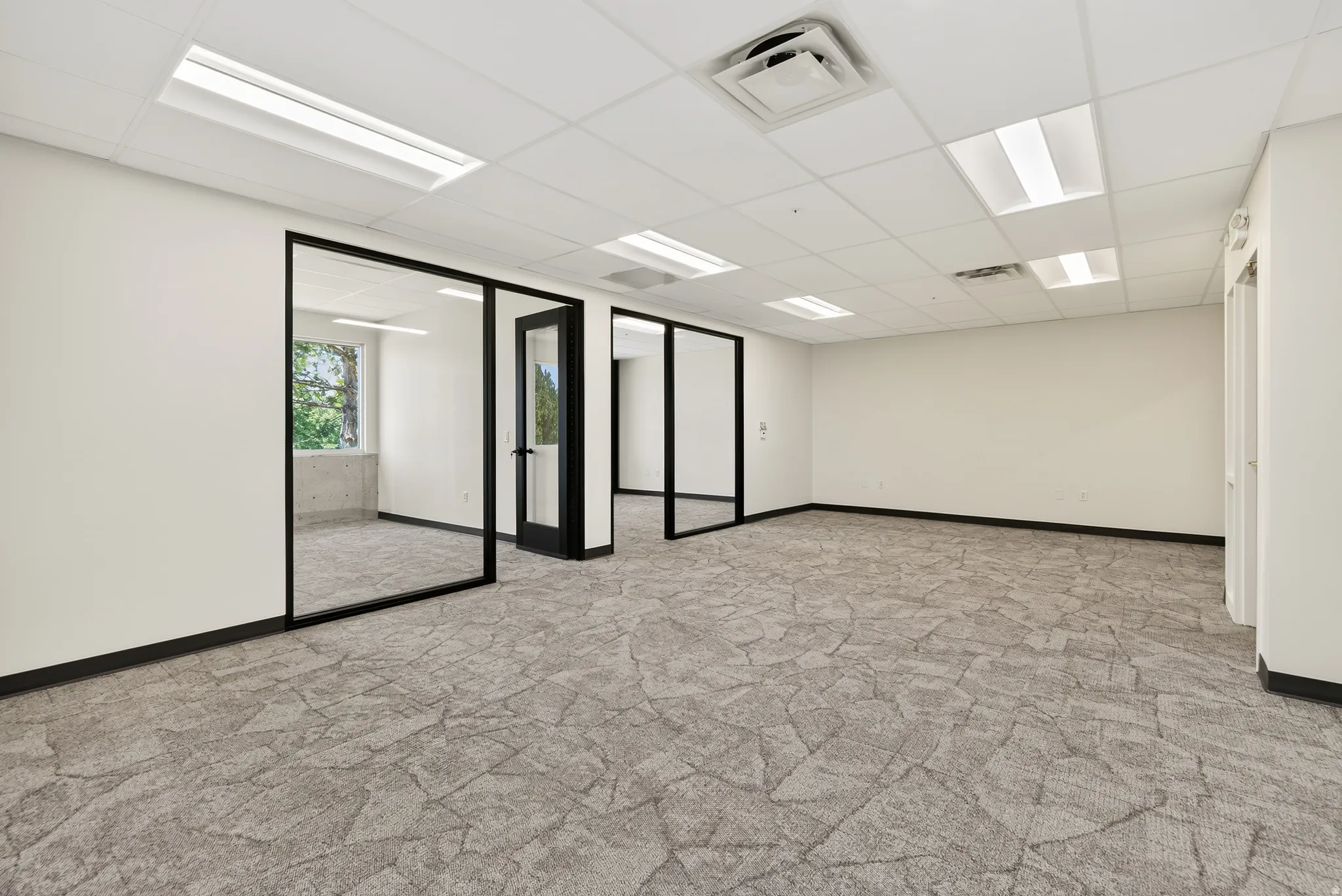 Open-plan interior with patterned carpet flooring, white walls, and a drop ceiling with recessed lighting